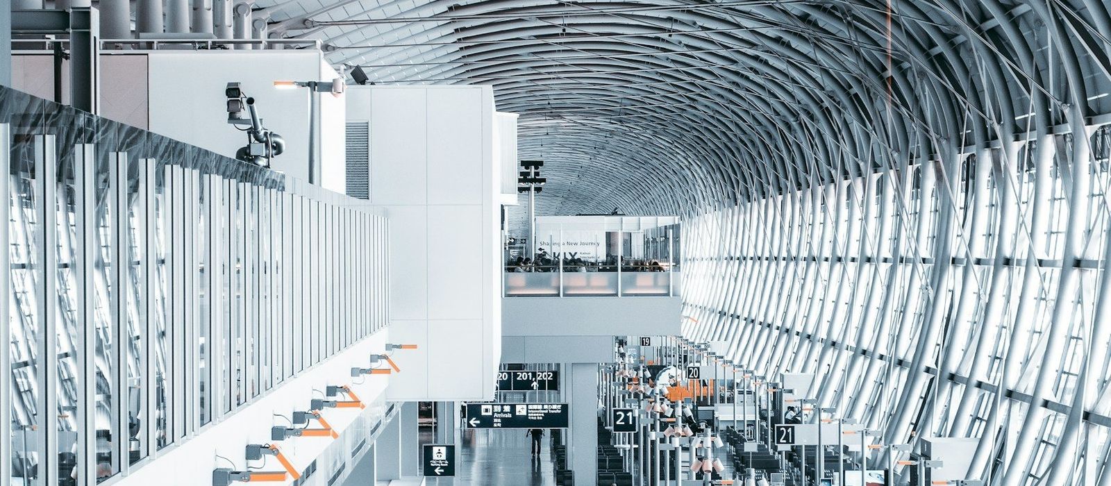 An airport terminal concourse under a vaulted steel-and-glass roof, with check-in rows and gate signage below